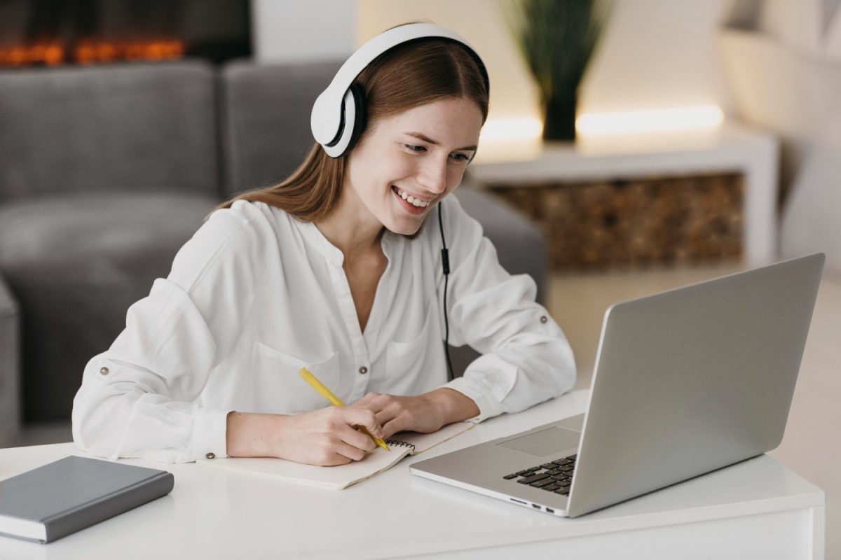 Adulto a assistir a aula online num portátil com caderno ao lado.