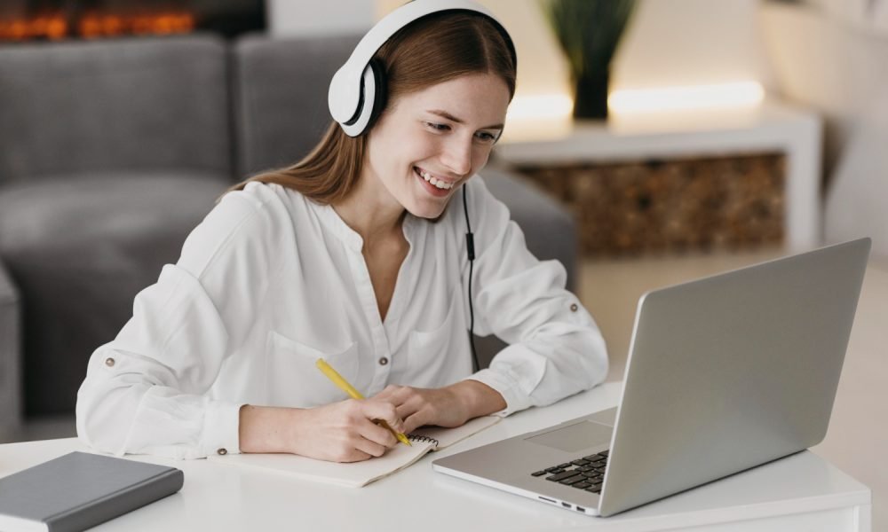 Adulto a assistir a aula online num portátil com caderno ao lado.